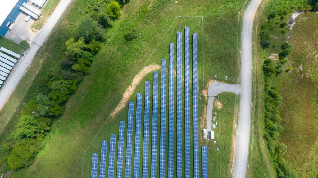 Aerial view showing a solar panel array in a lush rural landscape with a road.